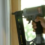 Man's hand using a pneumatic nailer on a window molding.