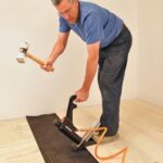 Man using a dead-blow hammer on a pneumatic nailer for hardwood flooring.