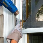 Man's hands heating and scraping old putty on window stile.