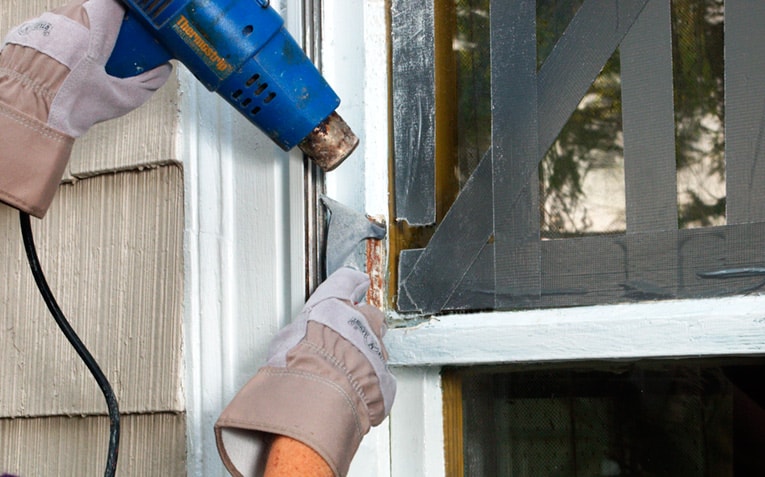 Man's hands heating and scraping old putty on window stile.