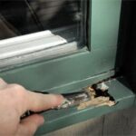 Man's hand removing rot on a window sill using a chisel.