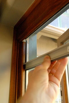 Man's hand pulling down a retractable window screen.