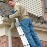 Man looking behind while standing on a step ladder, leaning on a rain gutter.