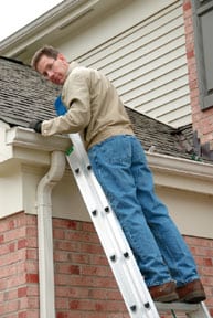 Man looking behind while standing on a step ladder, leaning on a rain gutter.