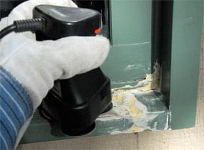 Man's hand sanding a dried epoxy wood filler in a window sill.