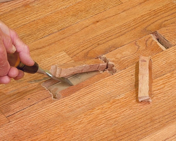 Man's hand, chiseling an end cut of a damaged wooden floor.
