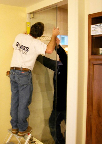 Two men installing a steam shower’s glass door inside a bathroom. 