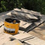 A bucket of asphalt roofing cement over a pile of roof tiles.