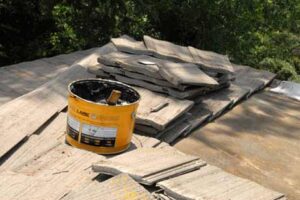 A bucket of asphalt roofing cement over a pile of roof tiles.