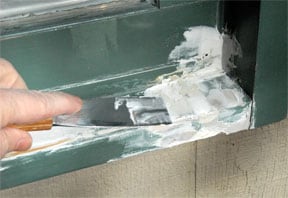 Man's hand applying vinyl compound on window sill using a putty knife.