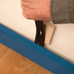 Man’s hand removing a blue base molding with a pry bar.