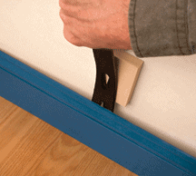 Man’s hand removing a blue base molding with a pry bar.