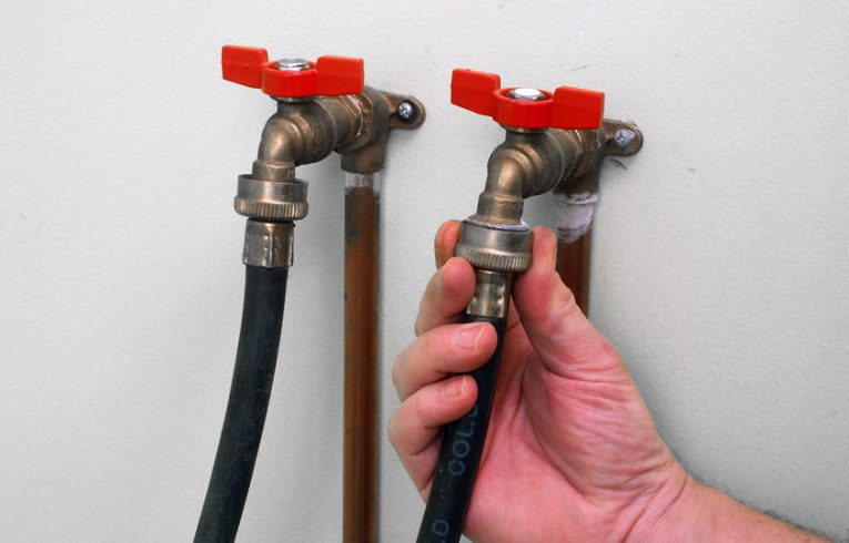 Man’s hand connecting a washer’s two hoses to water supply valves.