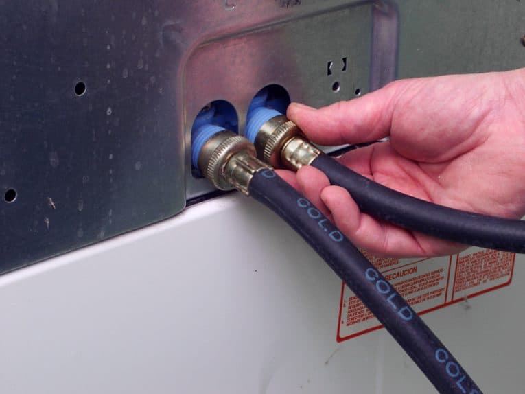 Man’s hand installing two labeled hoses at the back of a washer.