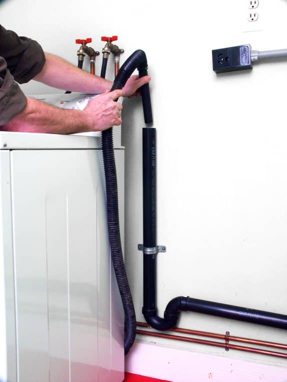 Man’s hands putting a washer’s drain hose in a standpipe.