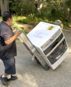 A man pushing a washer using a heavy-duty appliance hand truck.