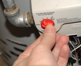 A hand adjusting a water heater temperature control dial.
