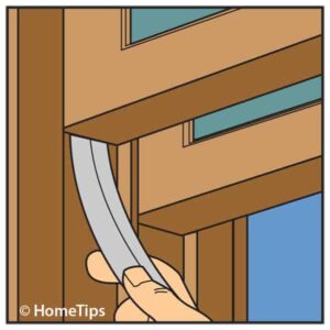 Diagram of a man’s hand inserting weather stripping between a window jamb and sash.