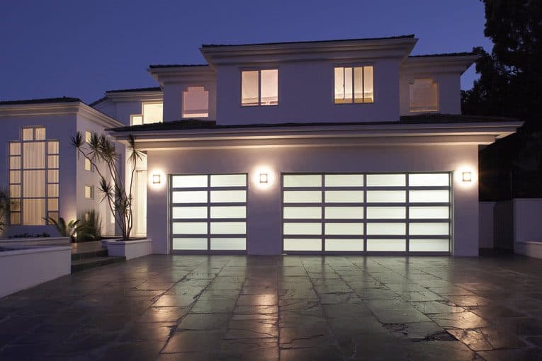 Two-story modern house’s front yard including outdoor lighting and a bright translucent, aluminum-framed, double door garage.