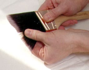 Man’s hand holding a paintbrush and spreading its bristles.