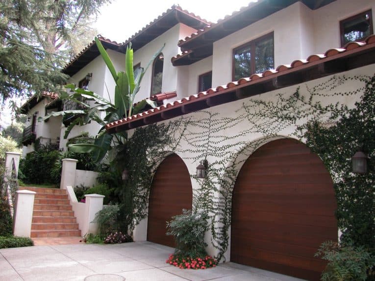 Two-story contemporary Mediterranean house’s front yard including a growing vine on an archway with a wooden double door garage.