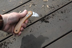 Man's hand removing debris between deck boards, using a laminate scoring tool.