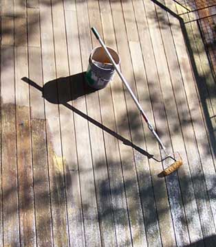 Refinishing a wood deck using a paint roller with an extension pole.