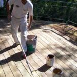 Man cleaning a wood deck, using a paint roller with an extension pole.