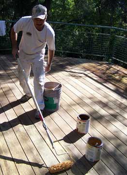 Man cleaning a wood deck, using a paint roller with an extension pole.