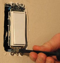Man's fingers screwing a light switch into a mounting slot.