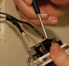 Man's hands unscrewing 2 wires at the back of the switch.