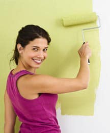 Woman looking behind while painting a wall using a roller.