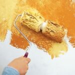 Man’s hand, rolling a two-part roller to create a yellow mottled finish.