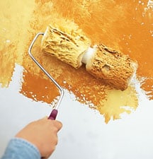 Man’s hand, rolling a two-part roller to create a yellow mottled finish.