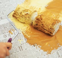 Man’s hand, rolling a two-part roller with paint on a newspaper.