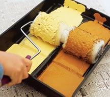 Man's hand, loading a two-part roller with paint on a dual tray.
