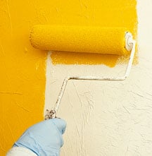 Man’s hand painting a wall with yellow using a roller.