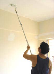 Man painting a ceiling using a roller attached to an extension pole.