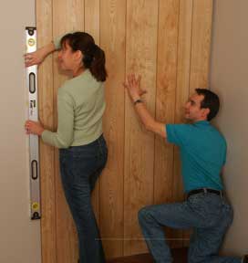 Man installing a wooden wall panel, including a woman doing spirit leveling.