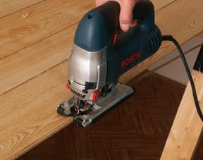 Man’s hand cutting a panel’s marked edge with a saber saw.