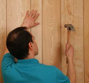 Man nailing a wooden wall panel.