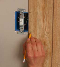 Man’s hand marking a wooden wall panel, beside an electrical box.