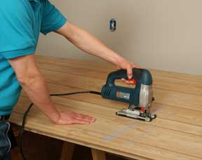 Man’s hands cutting a wooden panel with a saber saw.