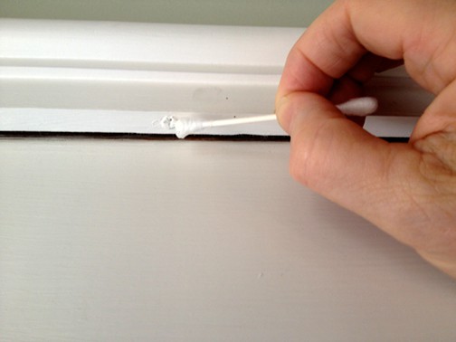 Man's hand removing paint on a screw head using a cotton bud.