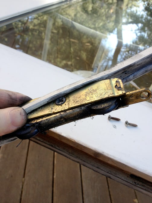 Man's hand pulling out a sliding door roller between a rubber weatherstripping.