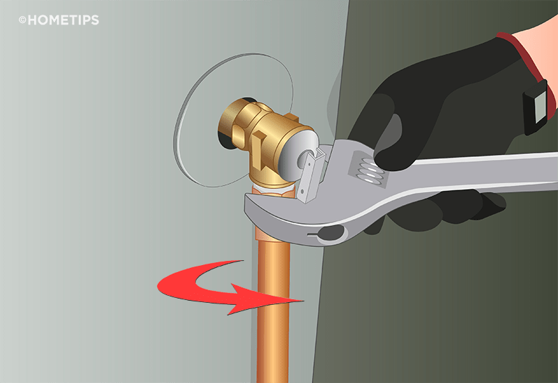 Gloved hand holding a wrench to screw the discharge pipe into a T&P valve, turning clockwise.