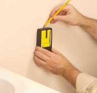 Man's hands holding a stud finder, while making marks on a wall.