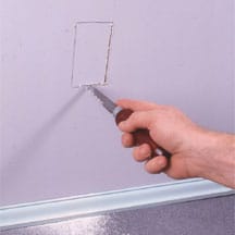 Man's hands cutting through a wall using a wallboard saw.