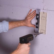 Man's hands screwing a mounting plate against a wall.