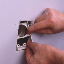 Man's hands pulling a mounting plate through a wall inlet hole.